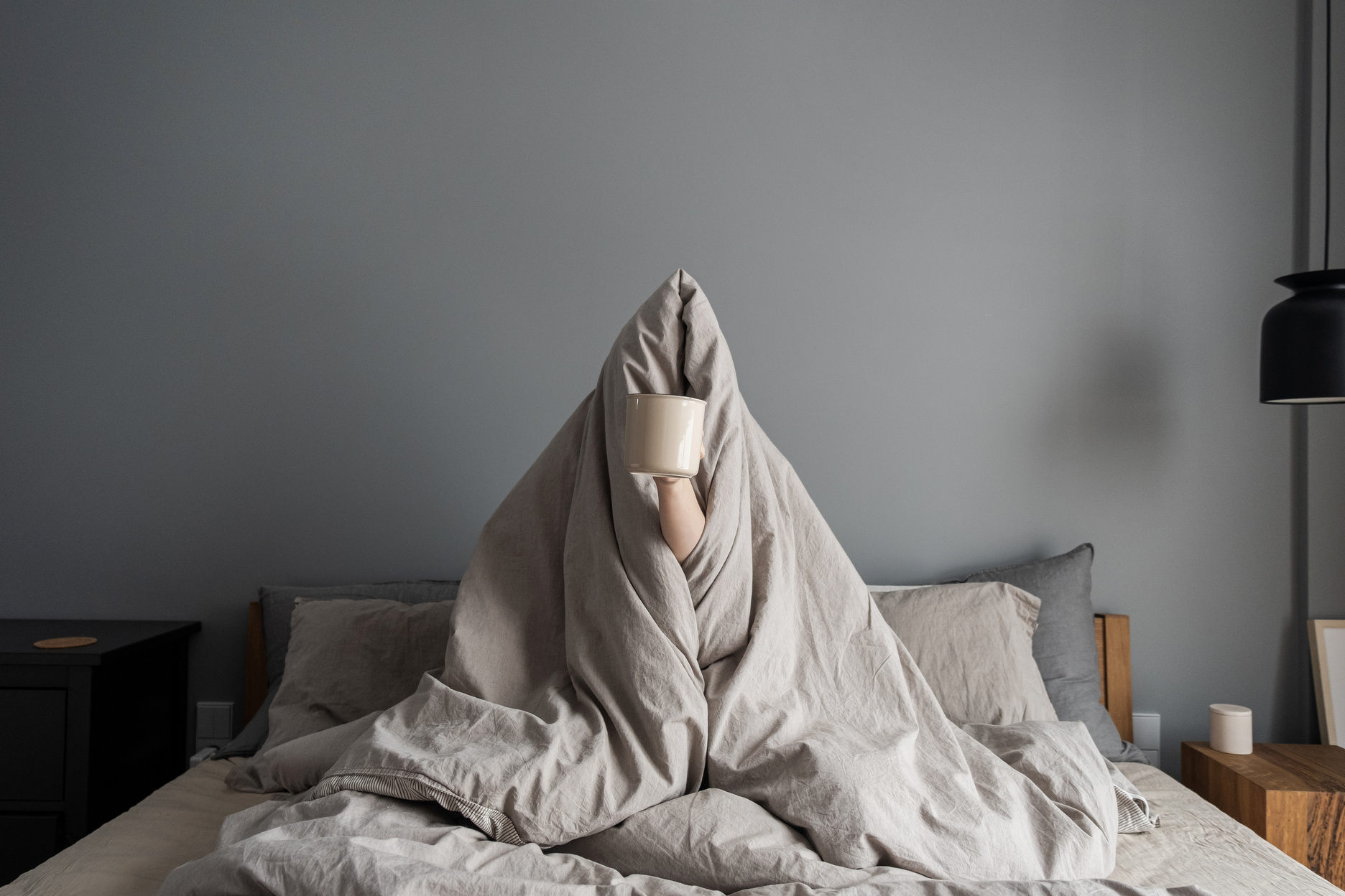 Woman Covered in Blanket Holding a Cup on the Bed